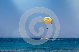 Skydiver flying with a yellow parachute by speed boat on sea. Skydiver control parachute down on surface of the sea