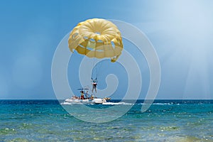 Skydiver flying with a yellow parachute by speed boat on sea. Skydiver control parachute down on surface of the sea