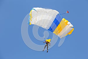 Skydiver under canopy of yellow with blue parachute in cloudless sky