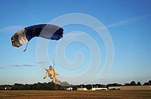 Skydiver under a small blue canopy of a parachute is landing on