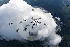A group of skydivers above white big cloud.