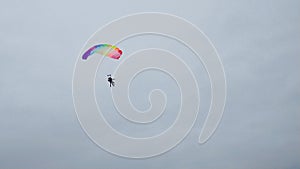 Skydivers with a multicolored parachute tandem in the air against a white sky