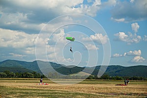 Skydiving landing, three parachutists, one of them is in the sky and the two of them on the ground