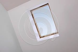 Skylight roof window and lamps on slanted ceiling in attic room, low angle view