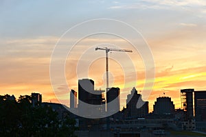 A skyline view of a city with a lifting crane in a construction site at sunset