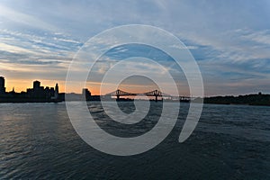 A skyline view a steel bridge across a river at the time between sunset and twilight. Jacques Cartier Bridge is across Saint