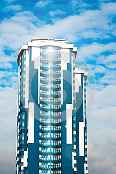 Skyscraper with a glass facade against a bright blue sky with figured clouds