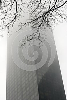 A skyscraper with the top disappearing in the fog, a moody  image of a gloomy day