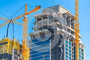 Skyscraper topoff with cranes on blue sky