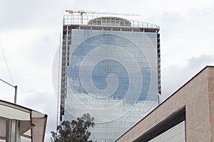 A Skyscraper under construction with blue windows reflects blue cloudy sky