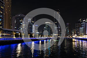 Skyscrapers illuminated by night reflected in water of canal. Dubai marina bay with yachts an boats timelapse hyperlapse