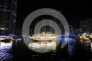 Skyscrapers illuminated by night reflected in water of canal. Dubai marina bay with yachts an boats timelapse hyperlapse