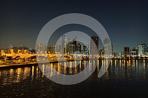 Skyscrapers are reflecting in water. Beautiful view to Sharjah city center lights skyline at night, United Arab Emirates