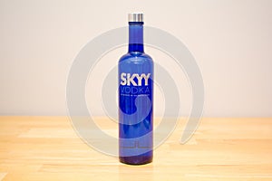 Skyy Vodka blue bottle on a wooden table with grey wall.