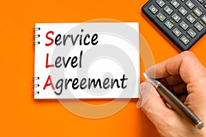 SLA service level agreement symbol. Concept words SLA service level agreement on beautiful white note. Beautiful orange background