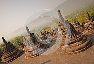 Slanted View of Borobudur Giant Stupas during late sunrise with misty feeling among the forest in the background