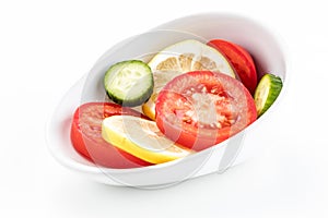 Slanted white bowl with circular yellow lemon red tomato and cucumber slices