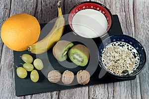 Slate board with a bowl of yogurt, a bowl of cereal and fruit on it