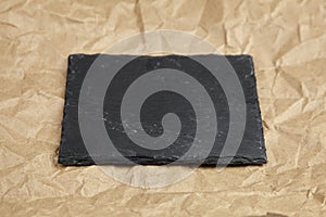 Slate board on crumpled craft paper background. Empty black stone serving board