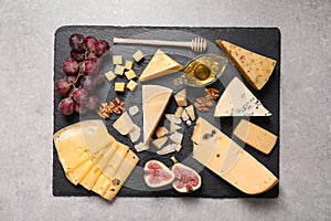 Slate board with different types of delicious cheese and snacks on grey table, top