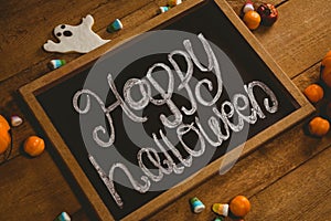 Slate with happy Halloween text by candies on wooden table