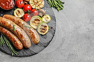 Slate plate with delicious barbecued sausages and vegetables on gray background.