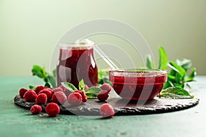 Slate plate with glass jar and bowl of tasty raspberry jam on green table