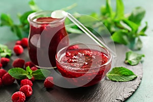 Slate plate with glass jar and bowl of tasty raspberry jam on green table