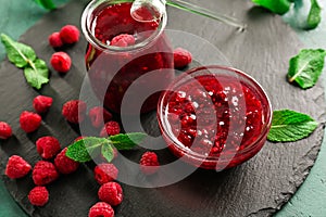 Slate plate with glass jar and bowl of tasty raspberry jam on green table