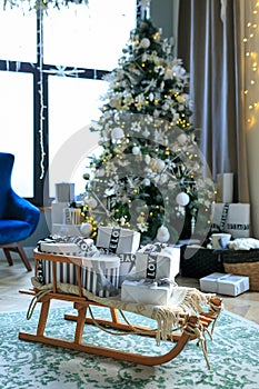 Sled loaded with gifts in room with Christmas decor and big windows. Christmas Room interior design, xmas tree decorated by lights
