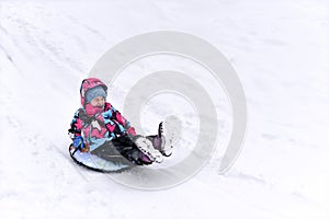 A sledding little girl on a hill against a winter landscape