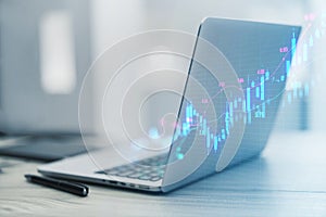 A sleek laptop projecting a virtual stock market chart, with pen and background