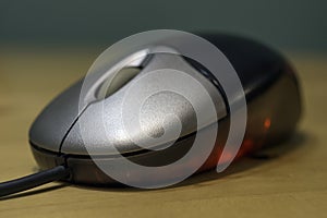 Sleek silver and black computer optical mouse with red light glowing against wooden desk table