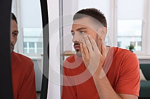 Sleep deprived man looking at himself in mirror indoors