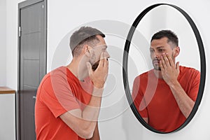 Sleep deprived man looking at himself in mirror indoors