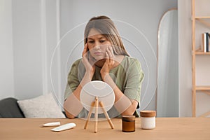 Sleep deprived young woman looking at herself in mirror indoors