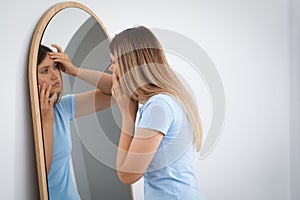 Sleep deprived young woman looking at herself in mirror indoors