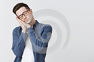 Sleep time. Tired attractive young man with pierced ear and glasses standing with closed eyes leaning on palms as pillow