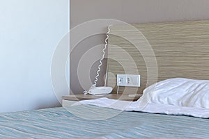 Sleeping area, bedroom in resort hotel with bed, bedside table, group of sockets and switch, telephone for contacting the