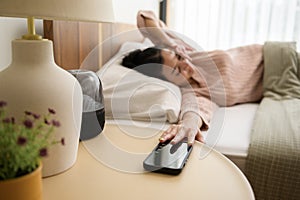 Sleeping asian woman turning off alarm on smartphone while being Waken up in the morning