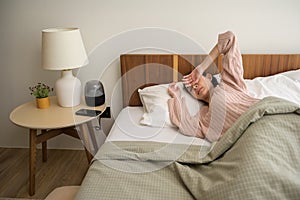 Sleeping asian woman turning off alarm on smartphone while being Waken up in the morning