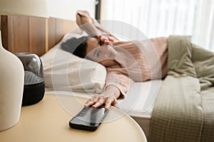 Sleeping asian woman turning off alarm on smartphone while being Waken up in the morning