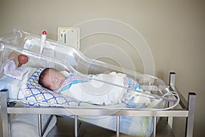 Happy newborn baby boy sleeping in a hospital room bed