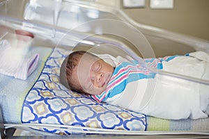 Happy newborn baby boy sleeping in a hospital room bed