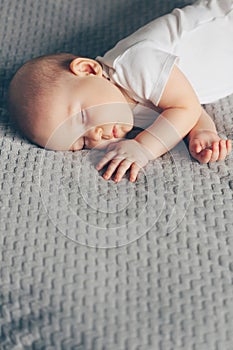 Sleeping baby boy in white bodysuit in bed with copyspace