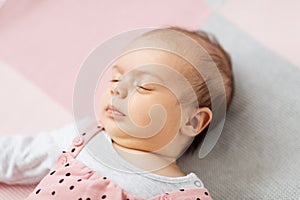 Sleeping baby girl in pink suit lying on blanket