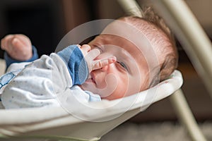 Sleeping baby in swing automatic electrical chair and sucking left thumb