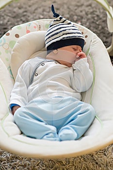 Sleeping baby in swing automatic electrical chair and sucking left thumb