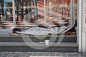 Sleeping bag of a homeless person spread on the stairs in front of a modern posh lounge or restaurant.