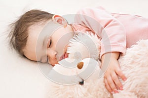 Sleeping beautiful baby toddler girl with a fluffy teddy bear on the bed, close-up portrait